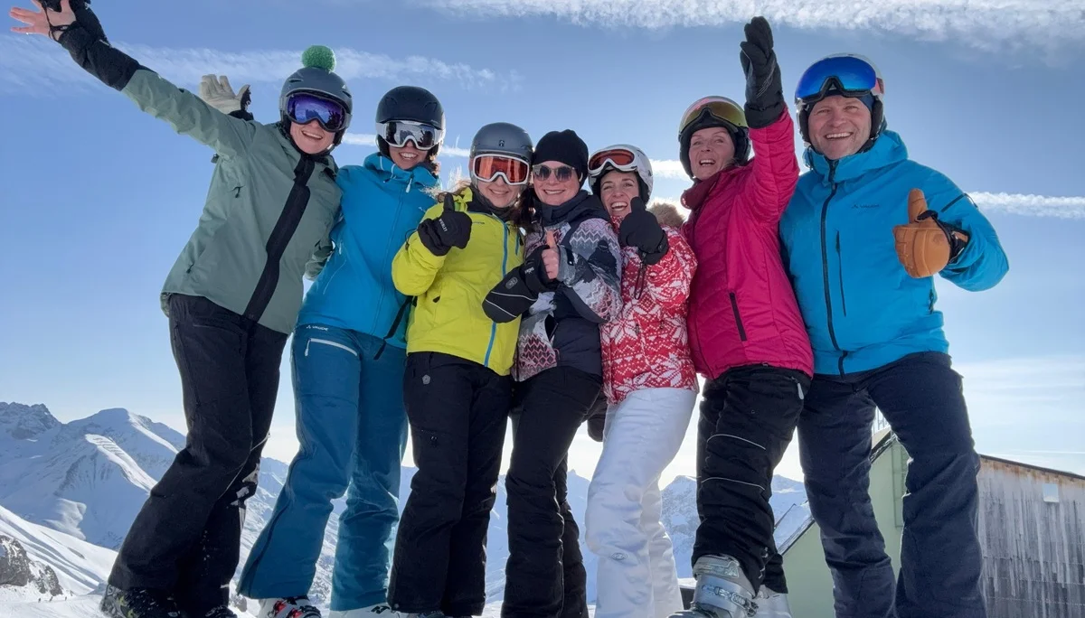 Gruppe von sechs Personen in bunter Skibekleidung steht auf Schnee vor Berglandschaft und Holzhütte, einige heben die Arme | © DAV-FN / V. u. S. Schmidhuber