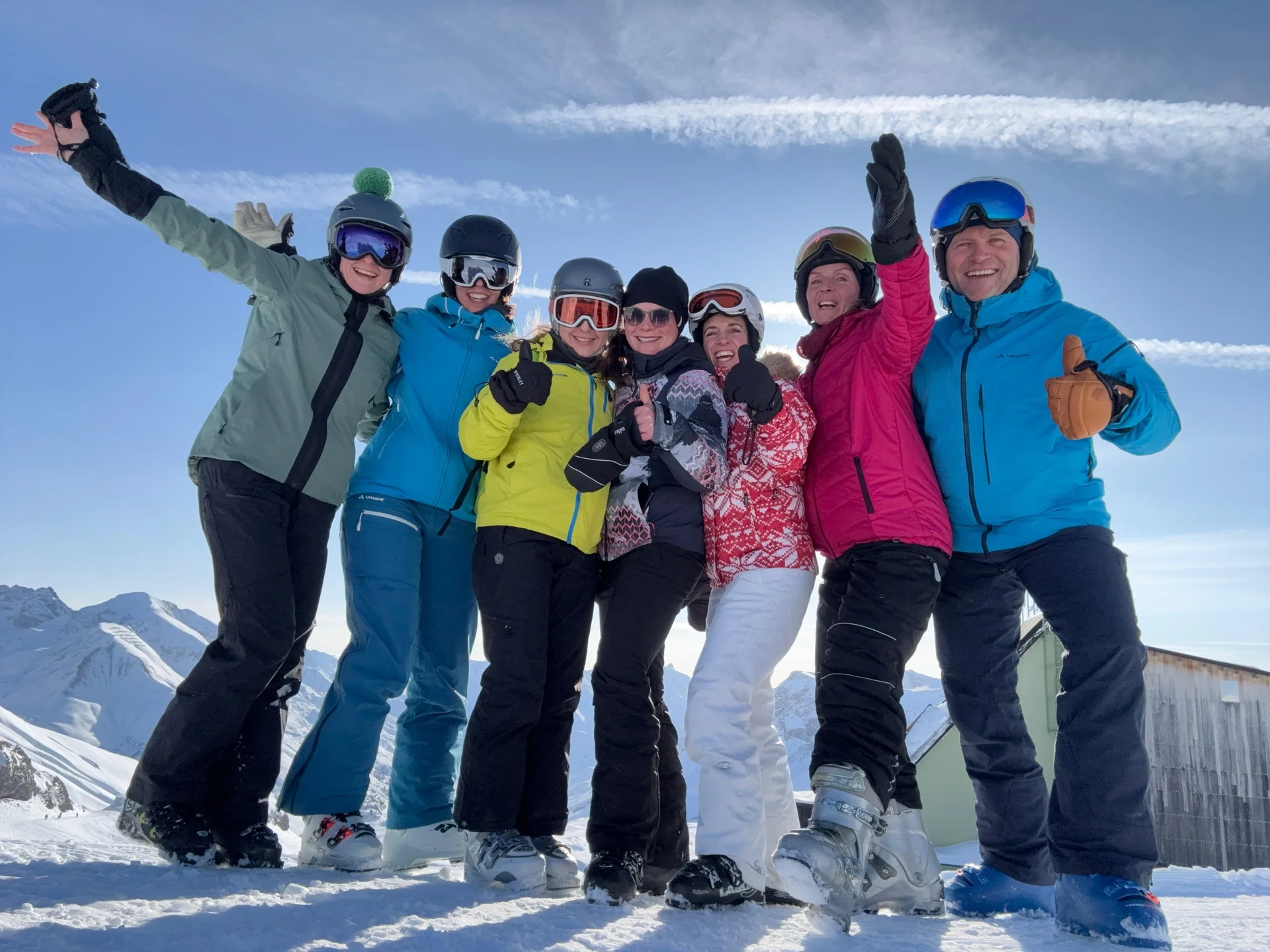 Gruppe von sechs Personen in bunter Skibekleidung steht auf Schnee vor Berglandschaft und Holzhütte, einige heben die Arme | © DAV-FN / V. u. S. Schmidhuber