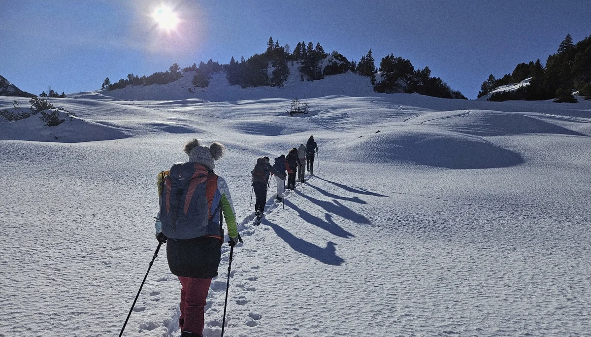 Gruppe von Wanderern mit Rucksäcken und Wanderstöcken steigt in einer verschneiten Berglandschaft bei Sonnenschein einen Hang hinauf | © DAV-FN / A. Schababerle