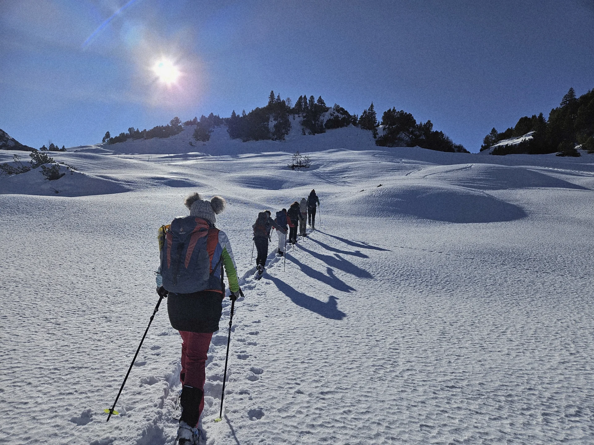 Gruppe von Wanderern mit Rucksäcken und Wanderstöcken steigt in einer verschneiten Berglandschaft bei Sonnenschein einen Hang hinauf | © DAV-FN / A. Schababerle