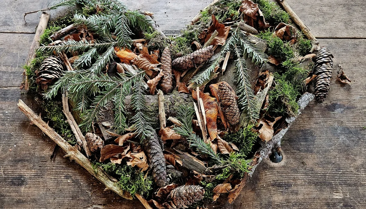 Herzförmige Anordnung aus Zweigen, Tannenzapfen, Moos und Blättern auf einer Holzfläche | © DAV-FN / A. Schababerle