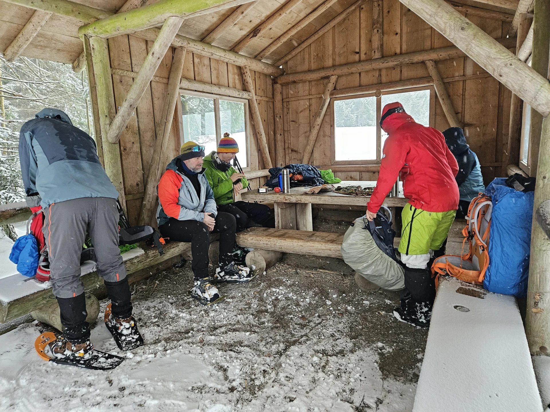 Mehrere Personen in Winterkleidung mit Schneeschuhen sitzen und stehen in einer hölzernen Schutzhütte mit Schneeboden | © DAV-FN / A. Schababerle