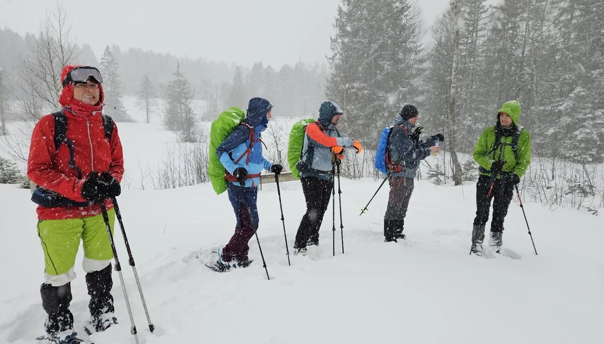 Fünf Personen mit Winterkleidung und Rucksäcken stehen mit Schneeschuhen und Wanderstöcken im tiefen Schnee vor verschneiten Bäumen | © DAV-FN / A. Schababerle