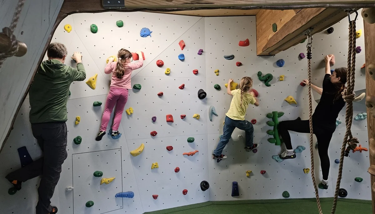 Vier Kinder klettern an einer Kletterwand mit bunten Griffen in einem Raum mit Holzbalken | © DAV-FN / A. Schababerle