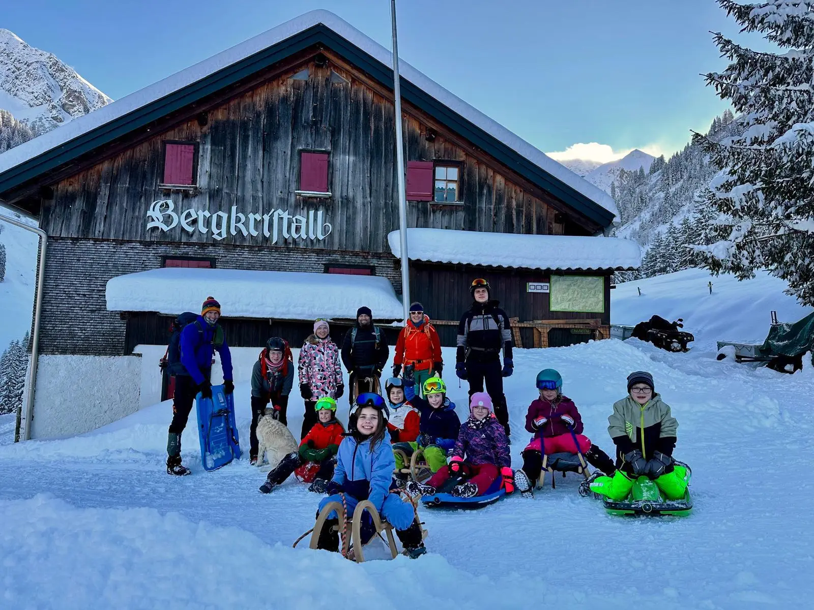 Gruppe von Kindern und Erwachsenen mit Schlitten vor einer Berghütte namens 'Bergkristall' in verschneiter Berglandschaft | © DAV-FN / A. Schababerle