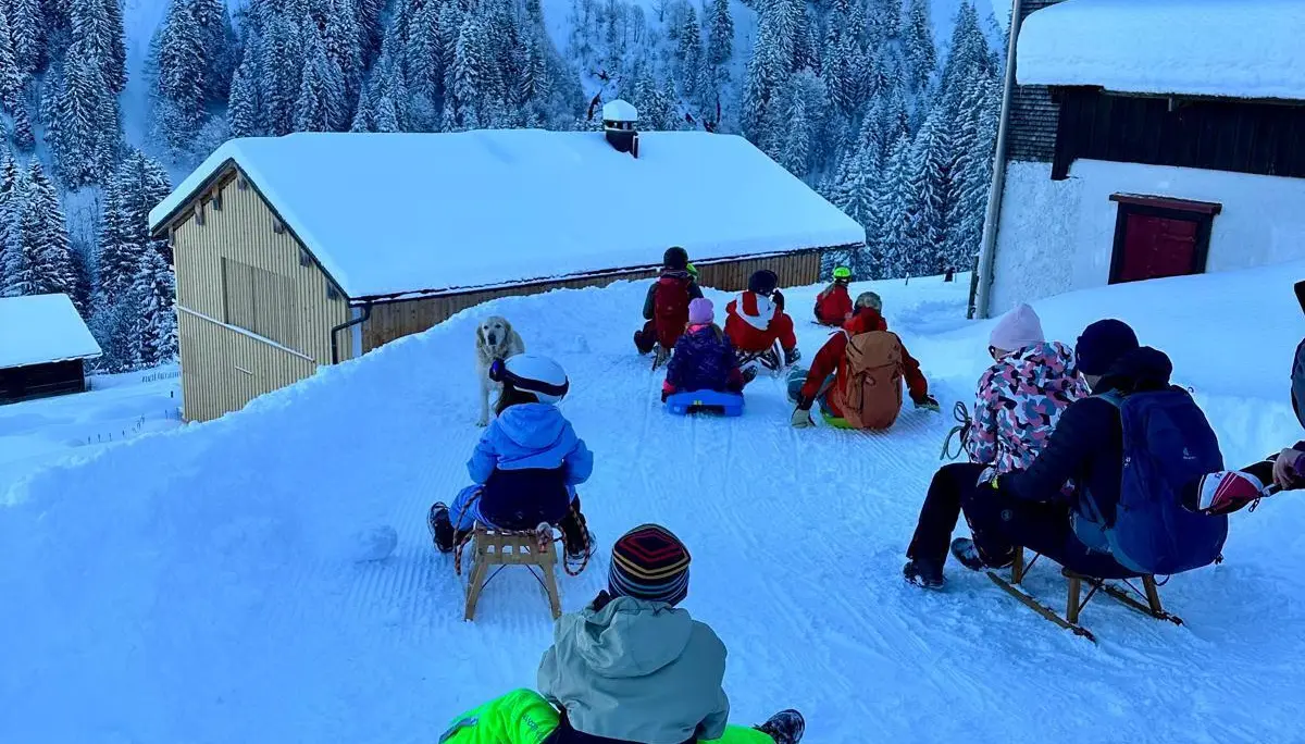 Gruppe von Kindern und Erwachsenen mit Schlitten vor einer Berghütte namens 'Bergkristall' in verschneiter Berglandschaft | © DAV-FN / A. Schababerle