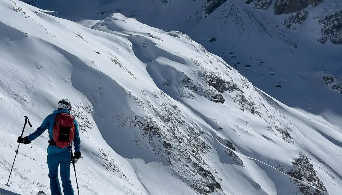 Skifahrer mit rotem Rucksack und blauer Kleidung auf verschneitem Hang vor steilen, schroffen Berggipfeln | © DAV-FN / S. Schmidhuber