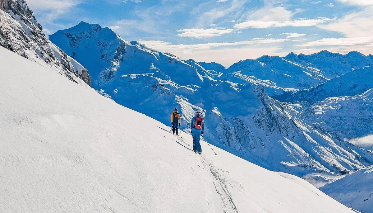 Zwei Personen mit Rucksäcken wandern auf einer schneebedeckten Bergflanke unter blauem Himmel | © DAV-FN / S. Schmidhuber