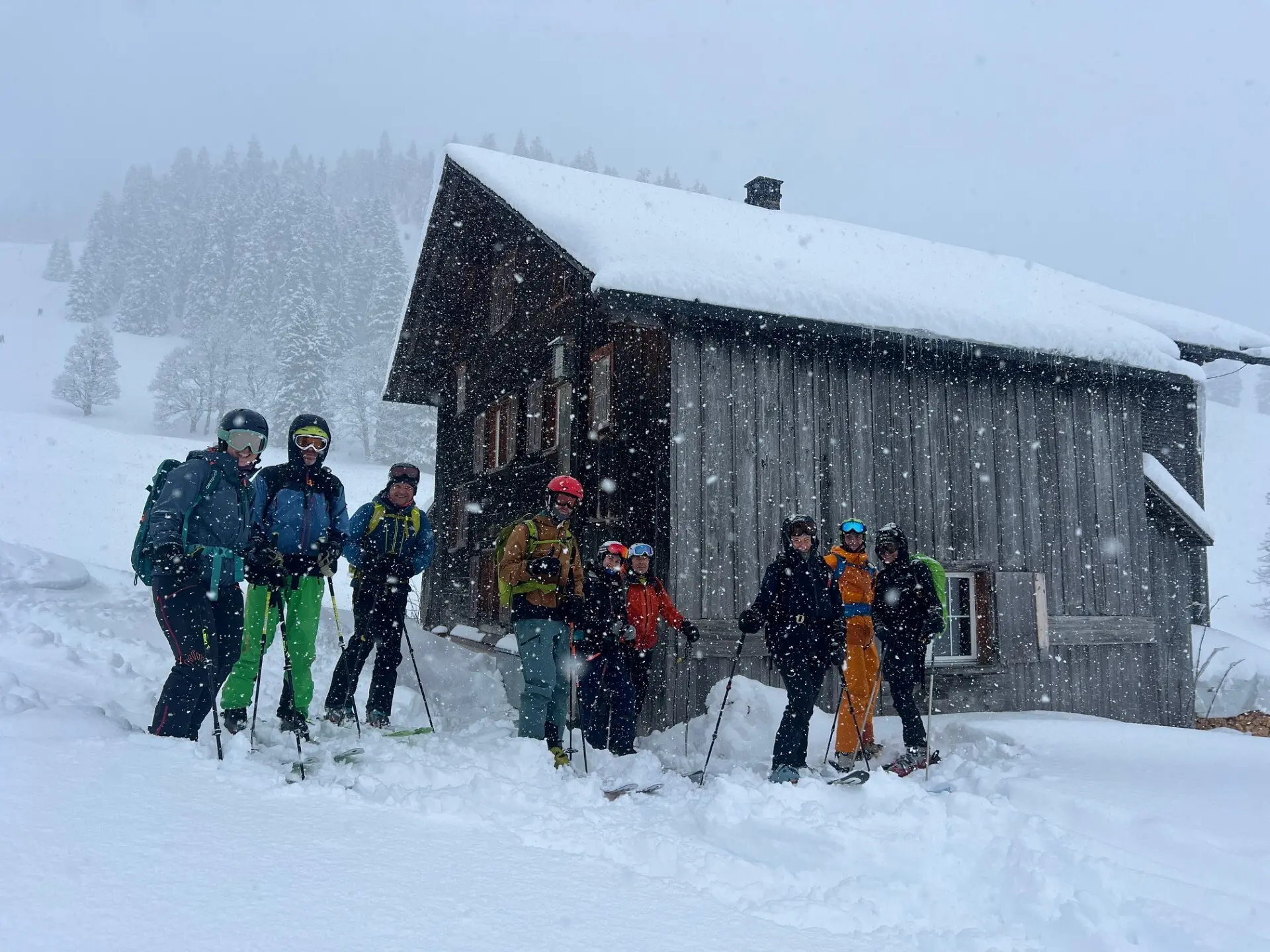 Gruppe von sieben Personen mit Skiausrüstung steht vor einer verschneiten Holzhütte in winterlicher Berglandschaft | © DAV-FN / C. + C. Ritter