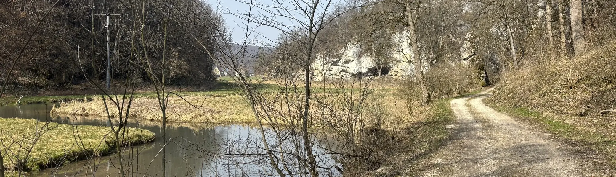Wanderweg entlang eines ruhigen Flusses mit kahlen Bäumen und Felsen im Hintergrund | © DAV-FN / A. Schech