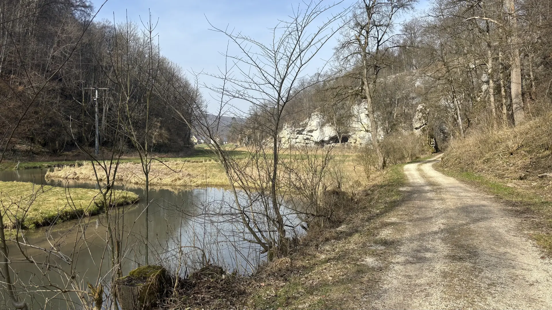 Wanderweg entlang eines ruhigen Flusses mit kahlen Bäumen und Felsen im Hintergrund | © DAV-FN / A. Schech