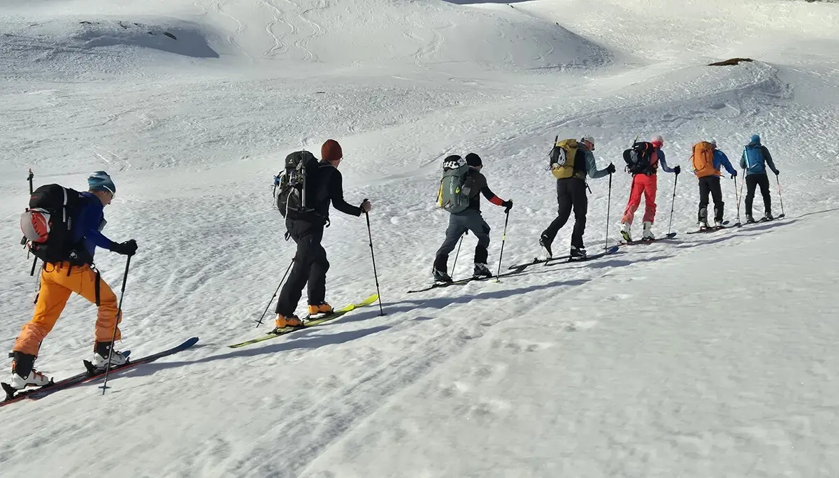 Sechs Skitourengehern mit Rucksäcken in einer Reihe auf verschneitem Hang | © DAV-FN / R. Lebedeff