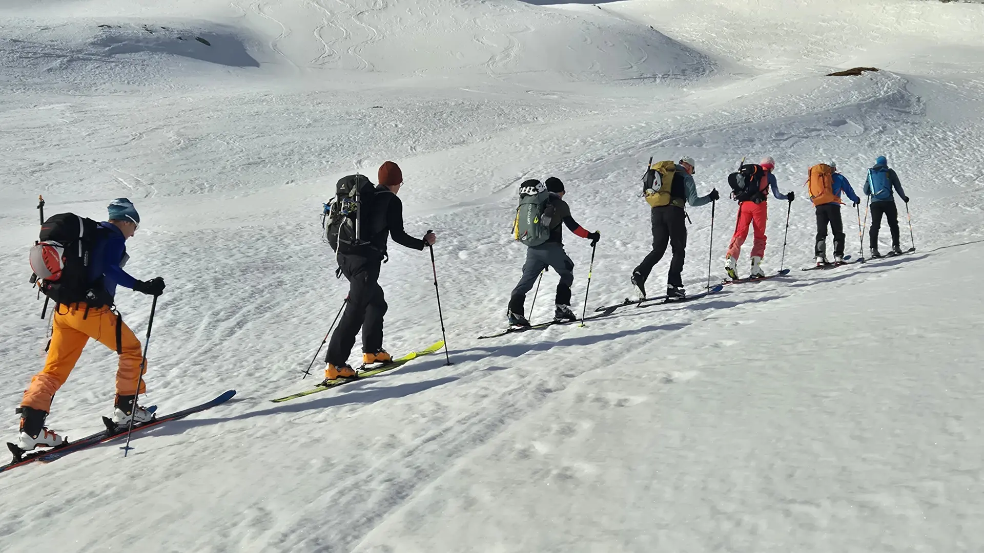 Sechs Skitourengehern mit Rucksäcken in einer Reihe auf verschneitem Hang | © DAV-FN / R. Lebedeff