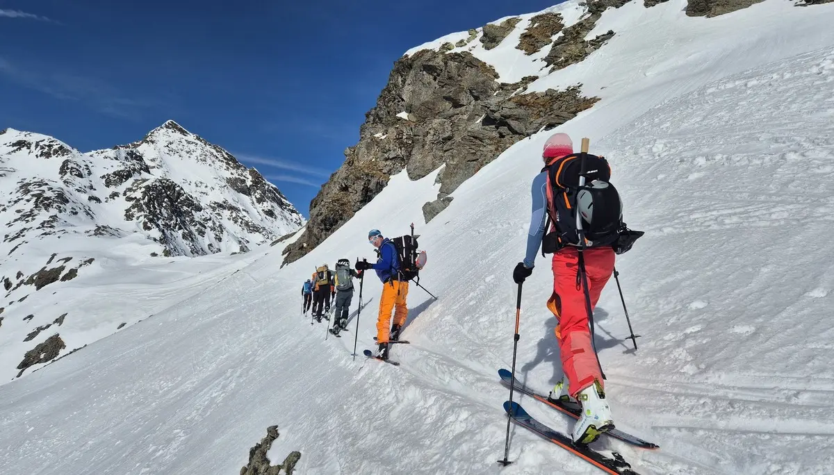 Gruppe von Skitourengehern steigt in einer schneebedeckten Berglandschaft mit steilem Hang und blauem Himmel auf | © DAV-FN / R. Lebedeff