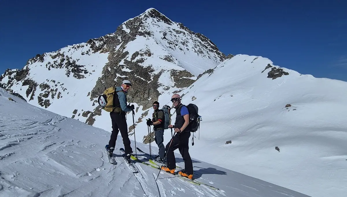 DreiSkitourengehern mit Rucksäcken stehen auf schneebedecktem Hang vor einem schneebedeckten Berg | © DAV-FN / R. Lebedeff