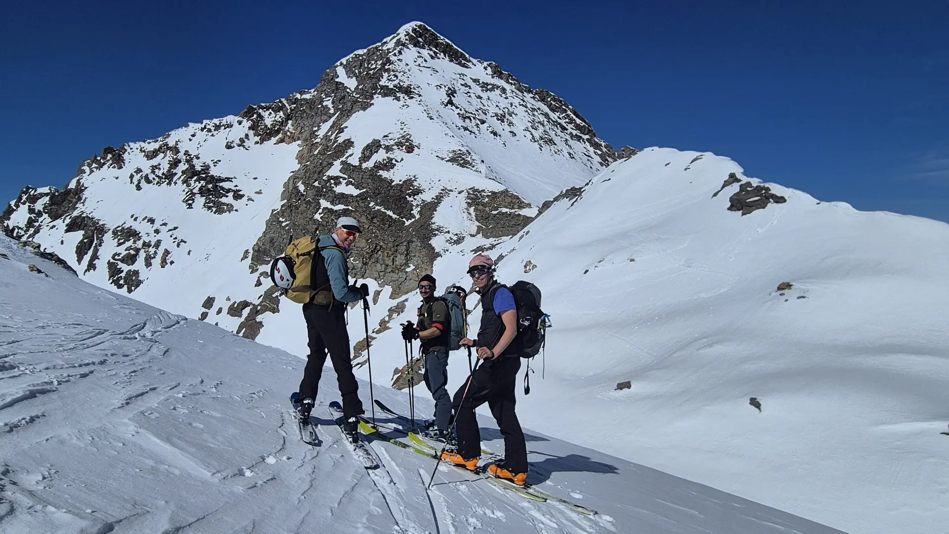DreiSkitourengehern mit Rucksäcken stehen auf schneebedecktem Hang vor einem schneebedeckten Berg | © DAV-FN / R. Lebedeff