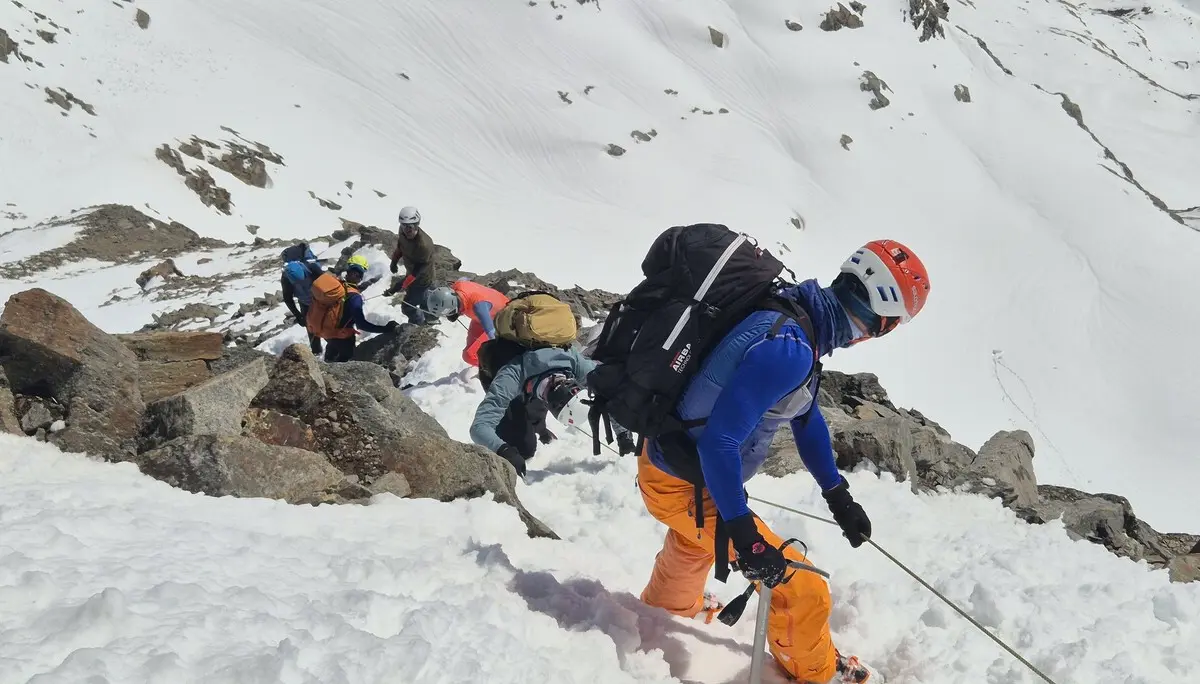 Gruppe von Bergsteigern mit Helmen und Rucksäcken klettert gesichert mit einem Fixseil einem schneebedeckten und felsendurchsetzten Berghang hinab. | © DAV-FN / R. Lebedeff
