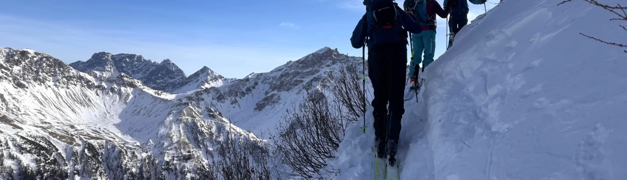 Drei Skitourengeher steigen auf einem schmalen, schneebedeckten Bergpfad mit Bergpanorama im Hintergrund auf | © DAV/Sandra Meyer