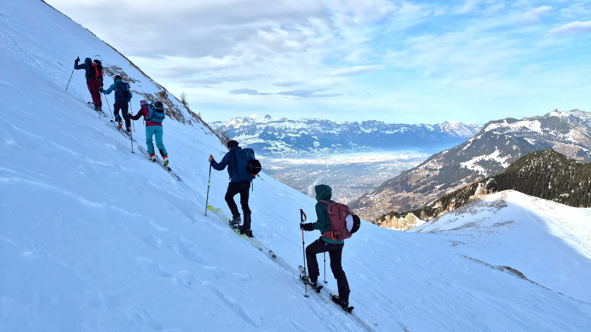 Gruppe von vier Personen mit Rucksäcken und Wanderstöcken steigt schräg einen schneebedeckten Hang in den Bergen hinauf | © DAV/Dirk Amos