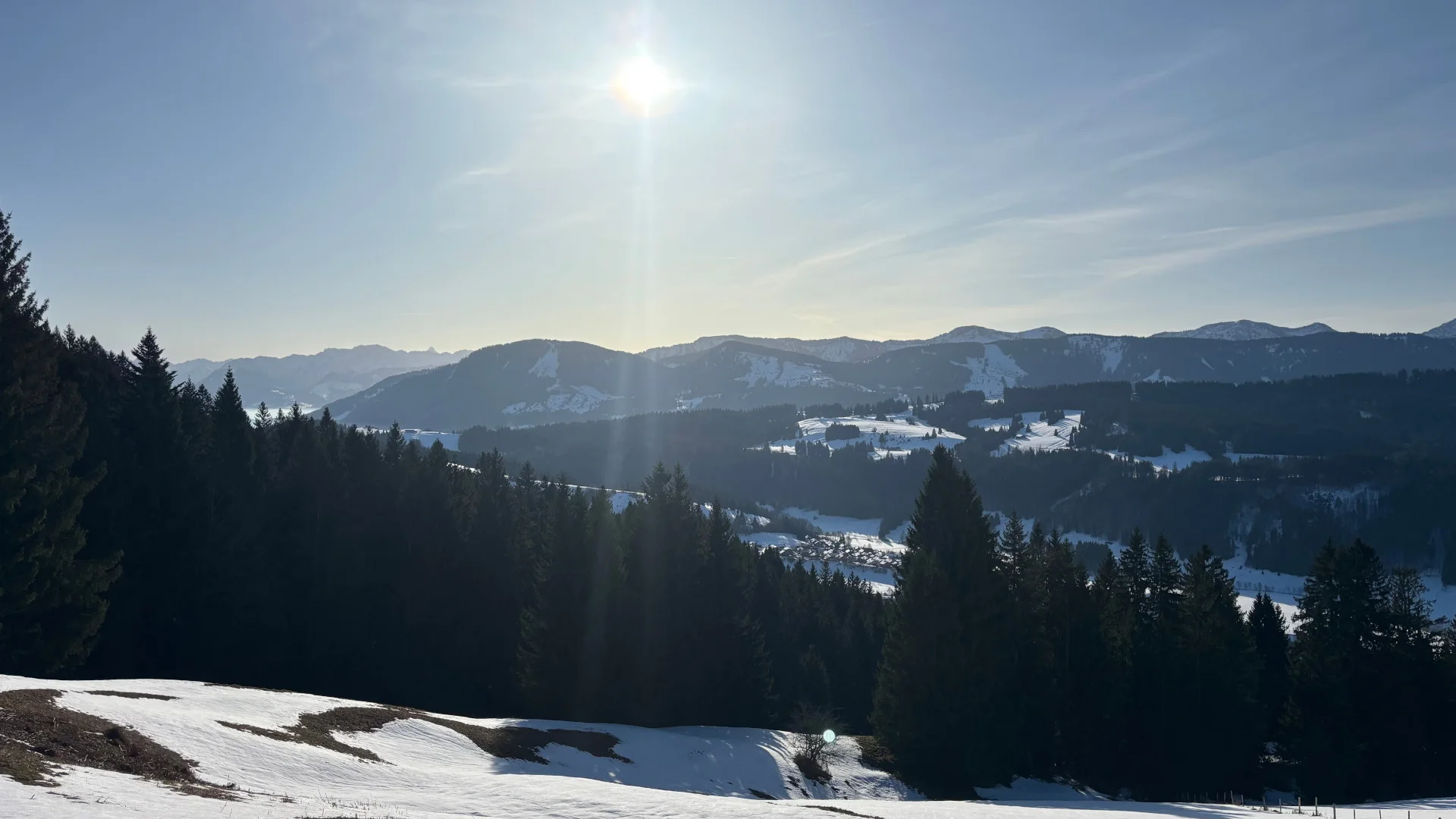 Landschaft mit schneebedeckten Hügeln, Tannenbäumen und Bergen im Hintergrund unter klarem Himmel mit Sonne | © DAV-FN / A. Schech