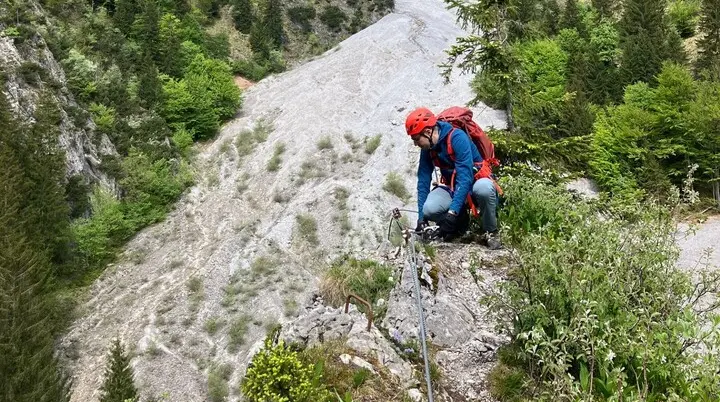 Bergsteiger mit Helm und Rucksack klettert an einem steilen Felsabhang in einem bewaldeten Gebirgstal | © DAV-FN / L. Fischer