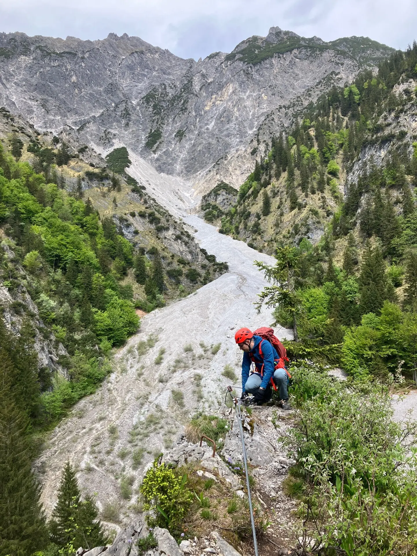 Bergsteiger mit Helm und Rucksack klettert an einem steilen Felsabhang in einem bewaldeten Gebirgstal | © DAV-FN / L. Fischer