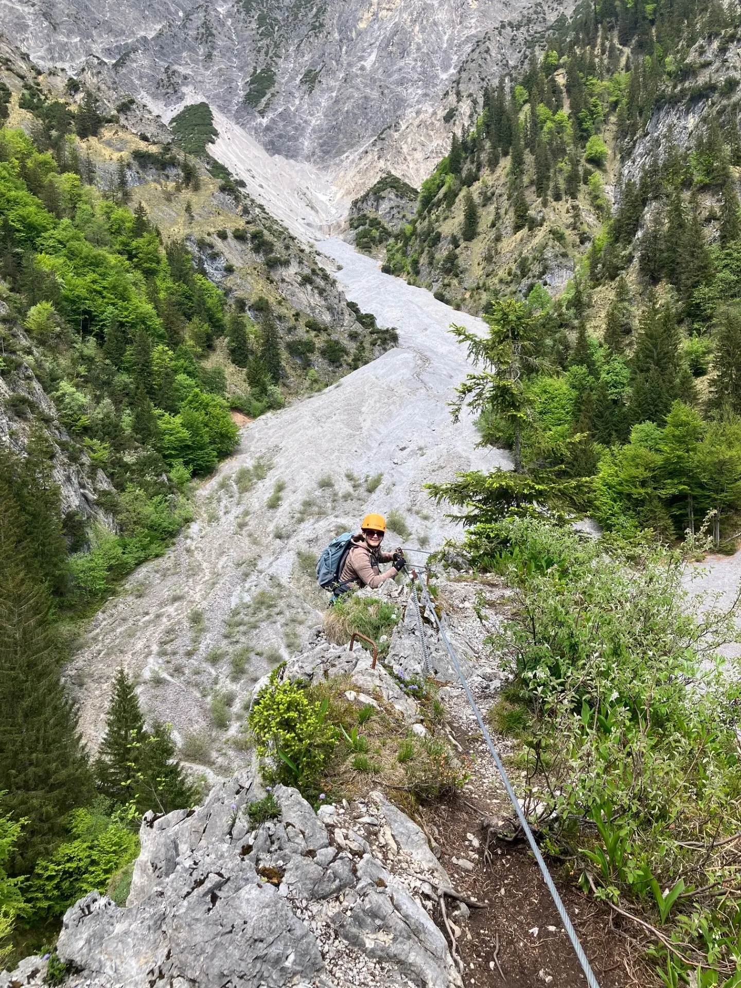 Bergsteiger mit Helm und Rucksack klettert an einem Stahlseil entlang eines steilen Felsgrats in einem bewaldeten Gebirgstal | © DAV-FN / L. Fischer