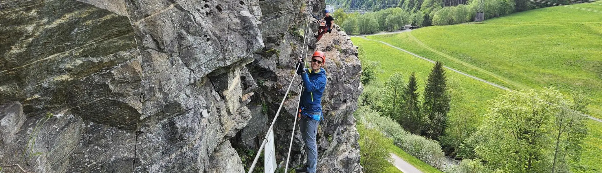 Zwei Personen klettern an einer Felswand mit Sicherungsseilen in einer grünen Berglandschaft | © DAV-FN / S. Meyer