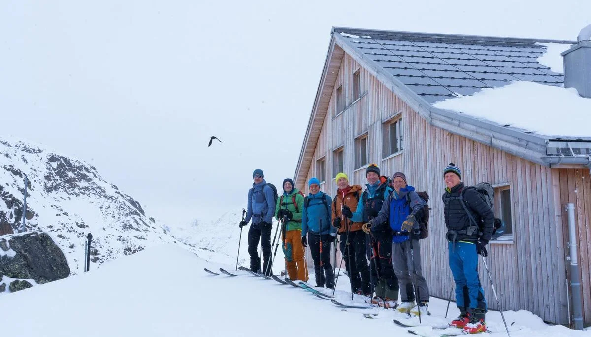 Gruppe von sieben Skifahrern mit Ausrüstung steht neben einem Holzhaus im verschneiten Gebirge. | © DAV-FN / B. Rayk
