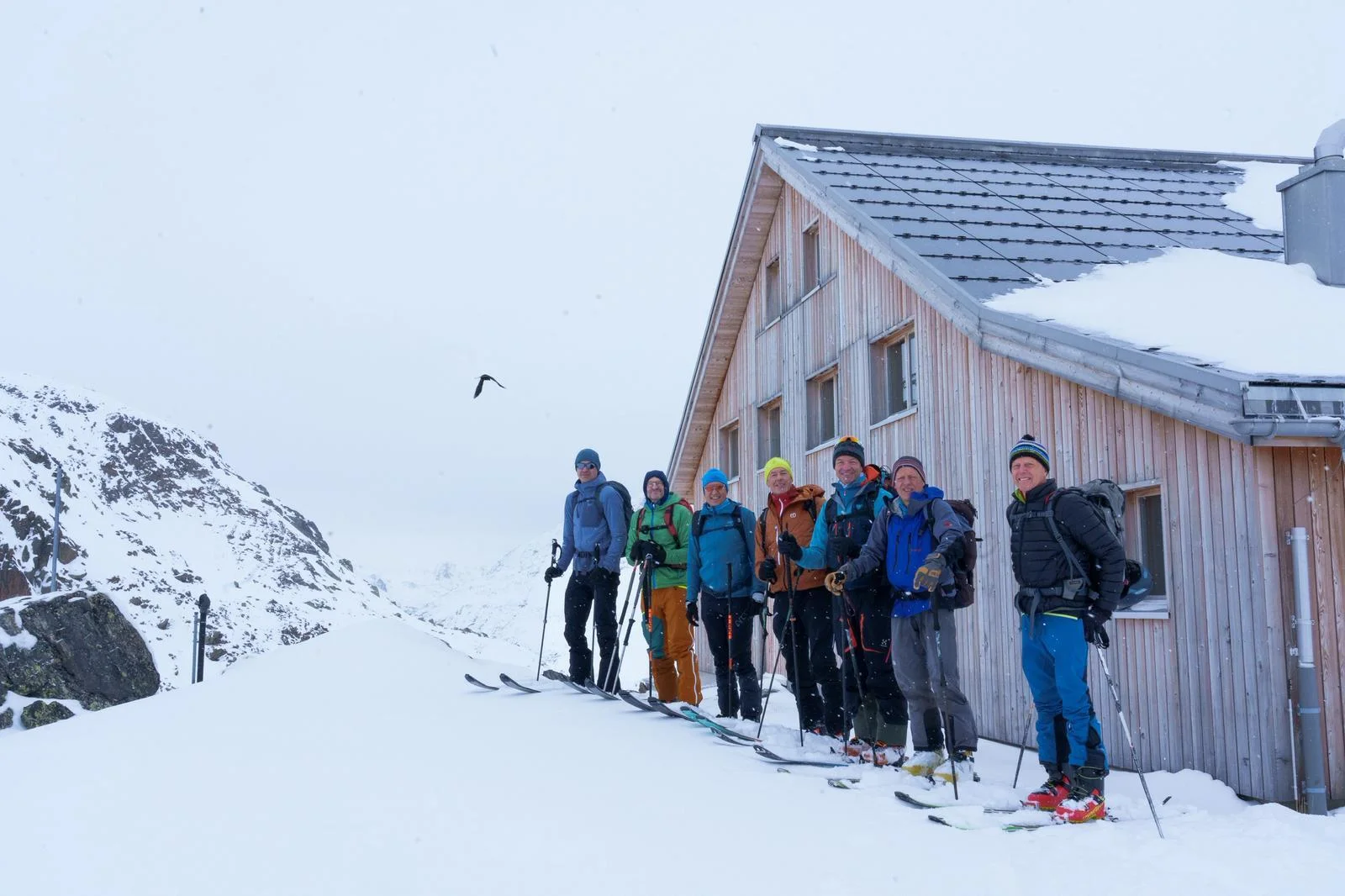 Gruppe von sieben Skifahrern mit Ausrüstung steht neben einem Holzhaus im verschneiten Gebirge. | © DAV-FN / B. Rayk