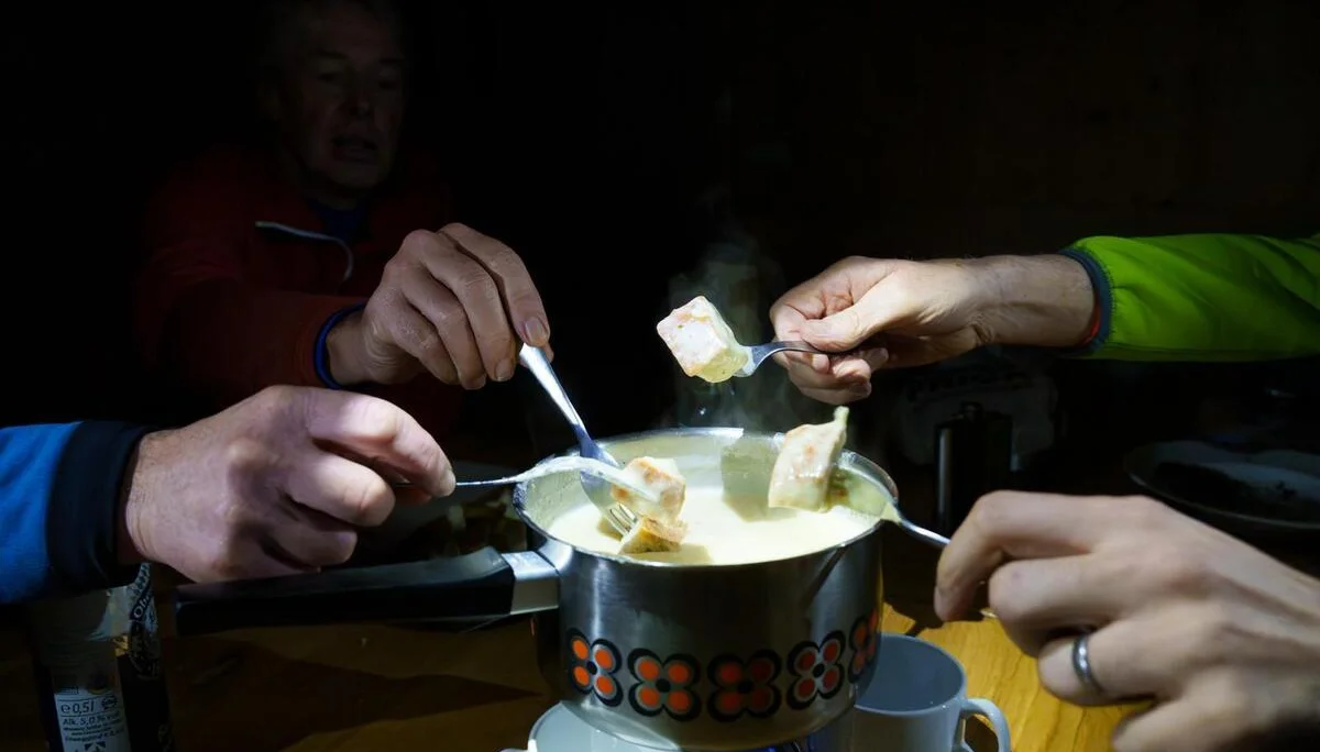 Mehrere Hände tauchen Brotstücke in einen dampfenden Käsefondue-Topf mit orange-schwarzem Muster. | © DAV-FN / B. Rayk