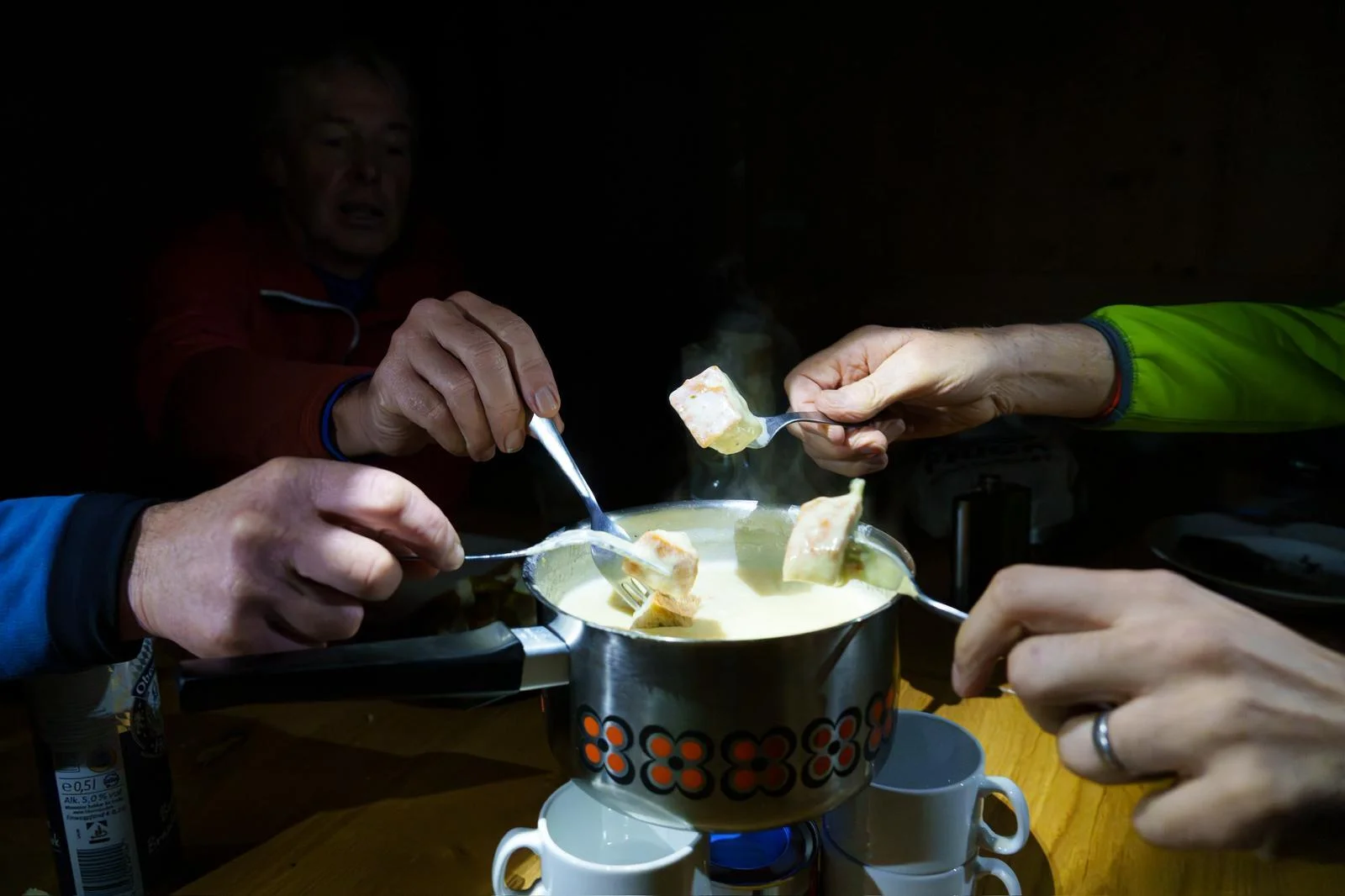 Mehrere Hände tauchen Brotstücke in einen dampfenden Käsefondue-Topf mit orange-schwarzem Muster. | © DAV-FN / B. Rayk