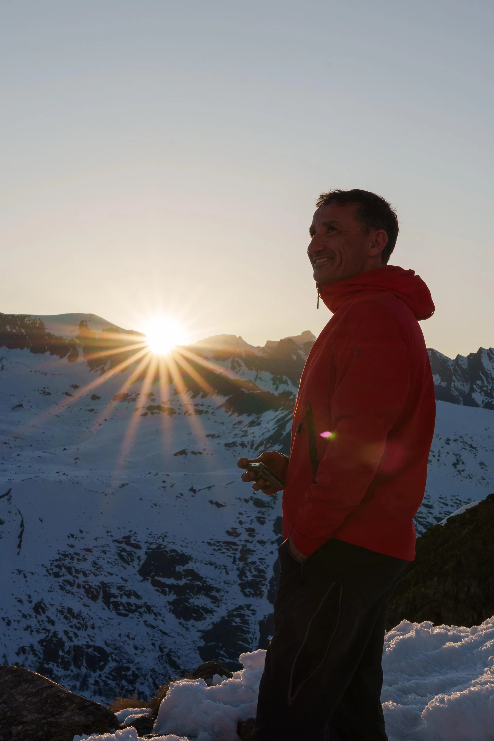 Mann in roter Jacke steht bei Sonnenuntergang vor verschneiten Bergen und hält ein GPS-Gerät in der Hand. | © DAV-FN / R. Gersten u. L. Chr. Fischer