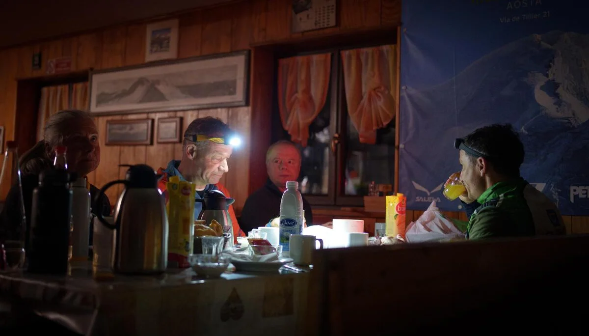 Drei Personen sitzen an einem Tisch mit Getränken und Snacks in einem rustikalen Raum mit Holzverkleidung und Vorhängen am Fenster | © DAV-FN / R. Gersten u. L. Chr. Fischer