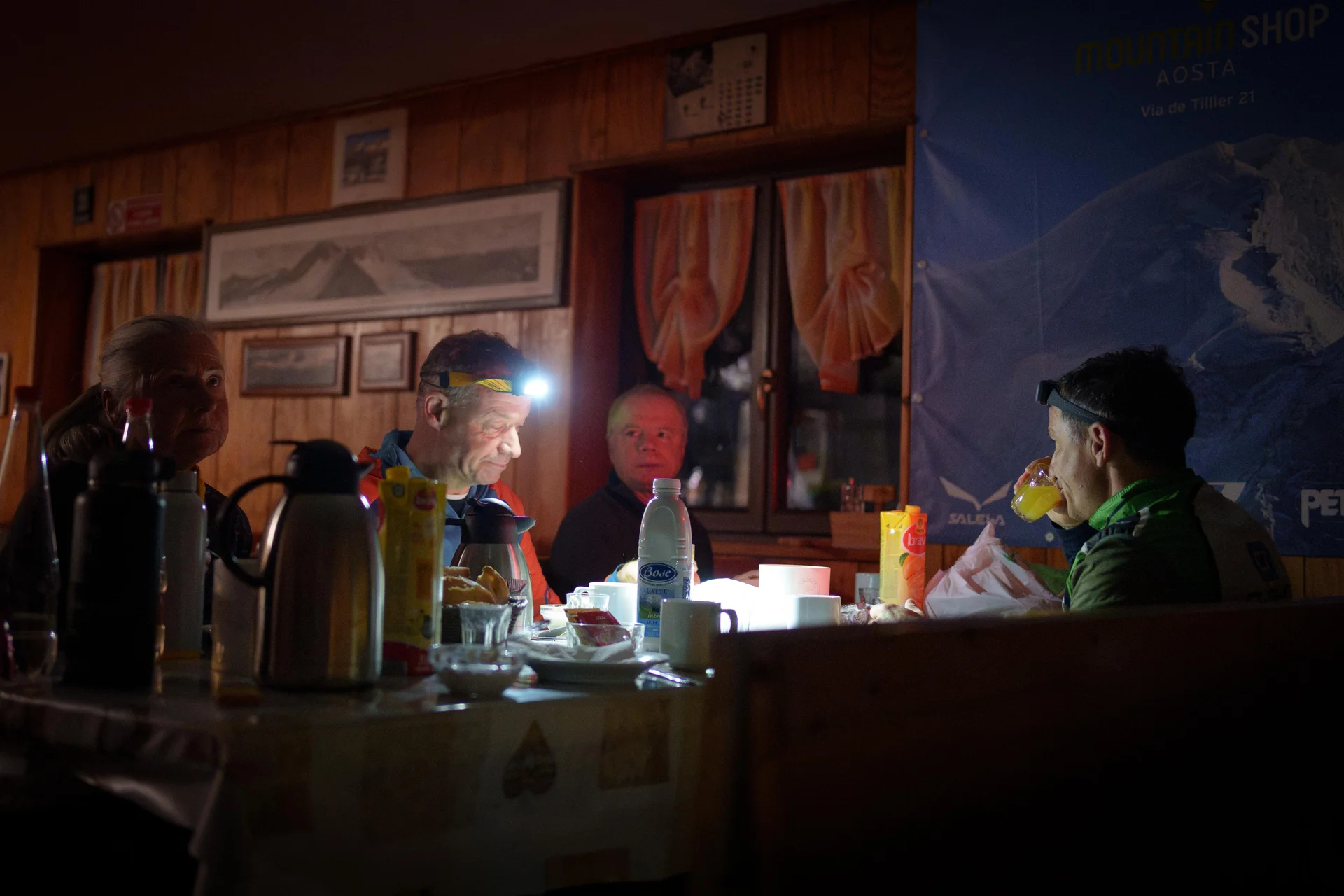 Drei Personen sitzen an einem Tisch mit Getränken und Snacks in einem rustikalen Raum mit Holzverkleidung und Vorhängen am Fenster | © DAV-FN / R. Gersten u. L. Chr. Fischer