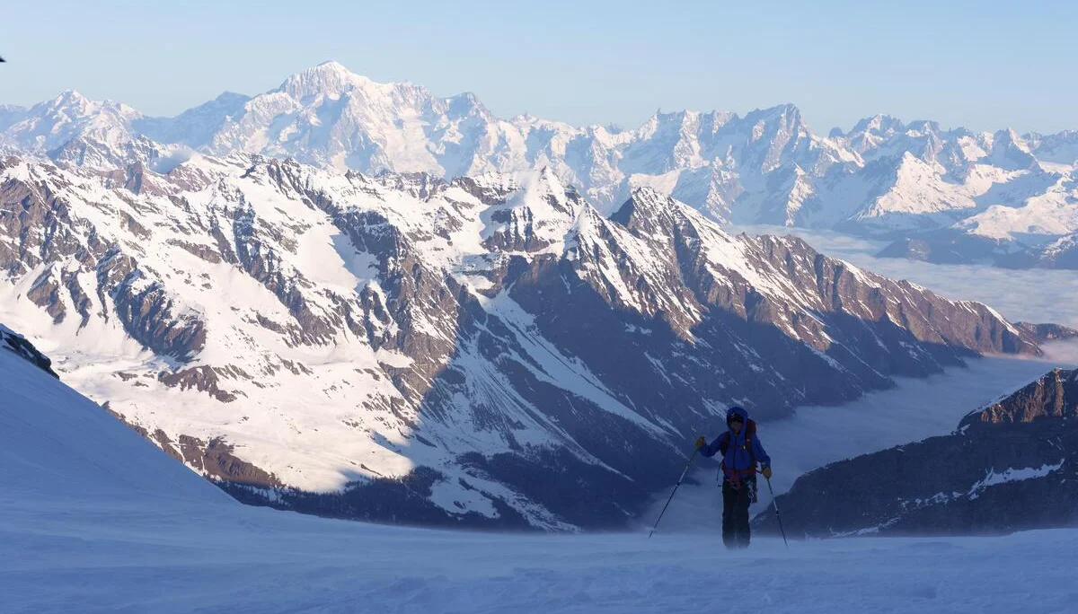 Skifahrer in blauer Jacke auf schneebedecktem Hang mit Blick auf schneebedeckte Alpenberge im Hintergrund | © DAV-FN / R. Gersten u. L. Chr. Fischer