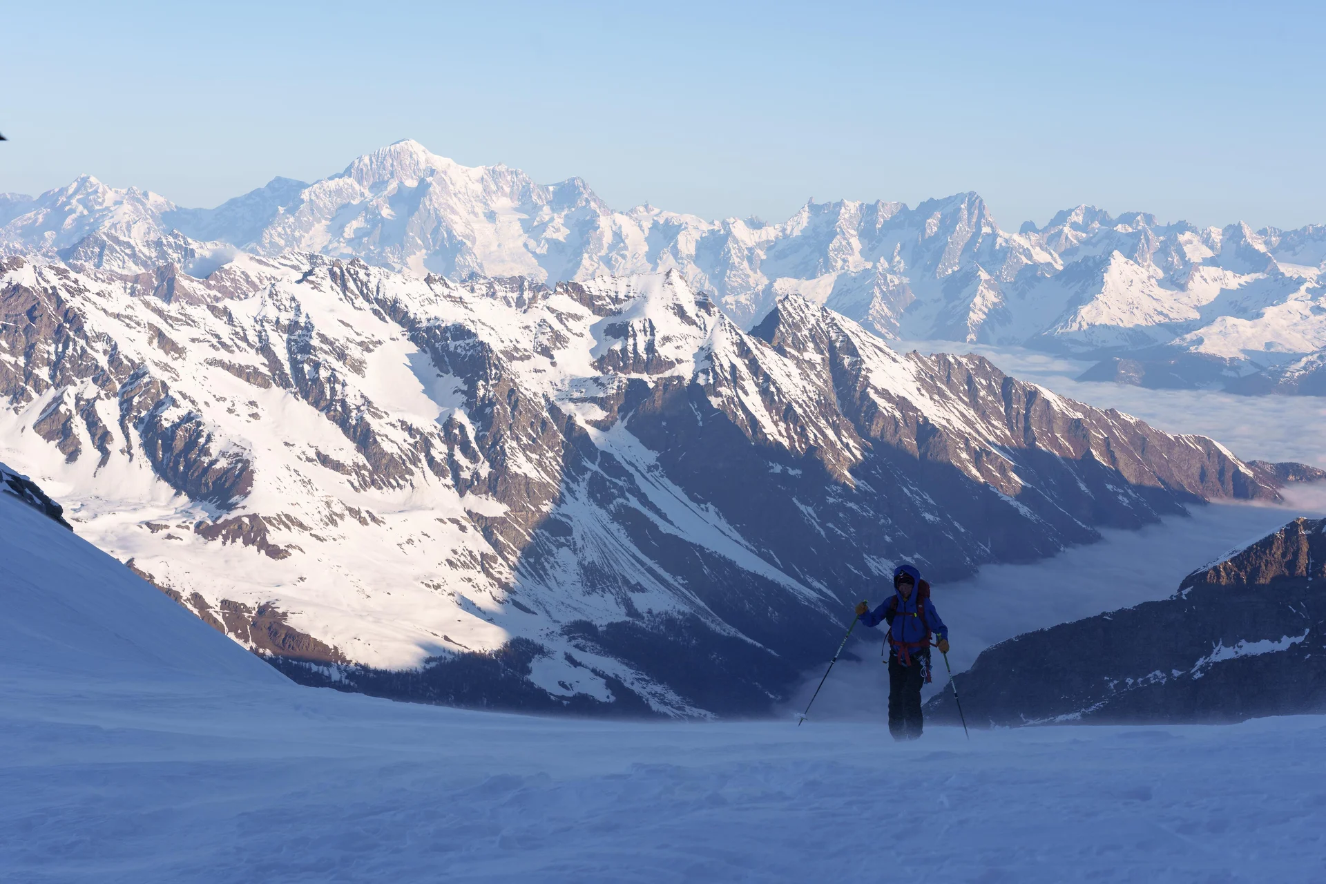 Skifahrer in blauer Jacke auf schneebedecktem Hang mit Blick auf schneebedeckte Alpenberge im Hintergrund | © DAV-FN / R. Gersten u. L. Chr. Fischer