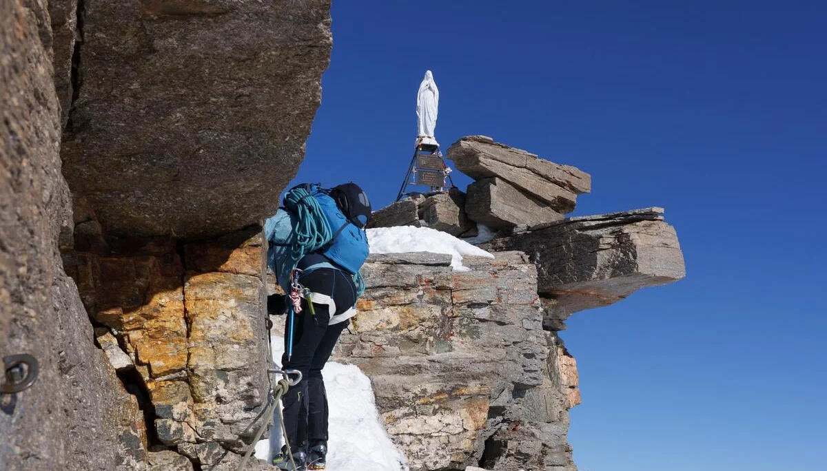 Bergsteiger mit blauem Rucksack klettert gesichert an steiler Felswand mit Schnee, Gipfel-Madonna des Gran Paradiso 4061m  im Hintergrund, Alpenpanorama | © DAV-FN / R. Gersten u. L. Chr. Fischer