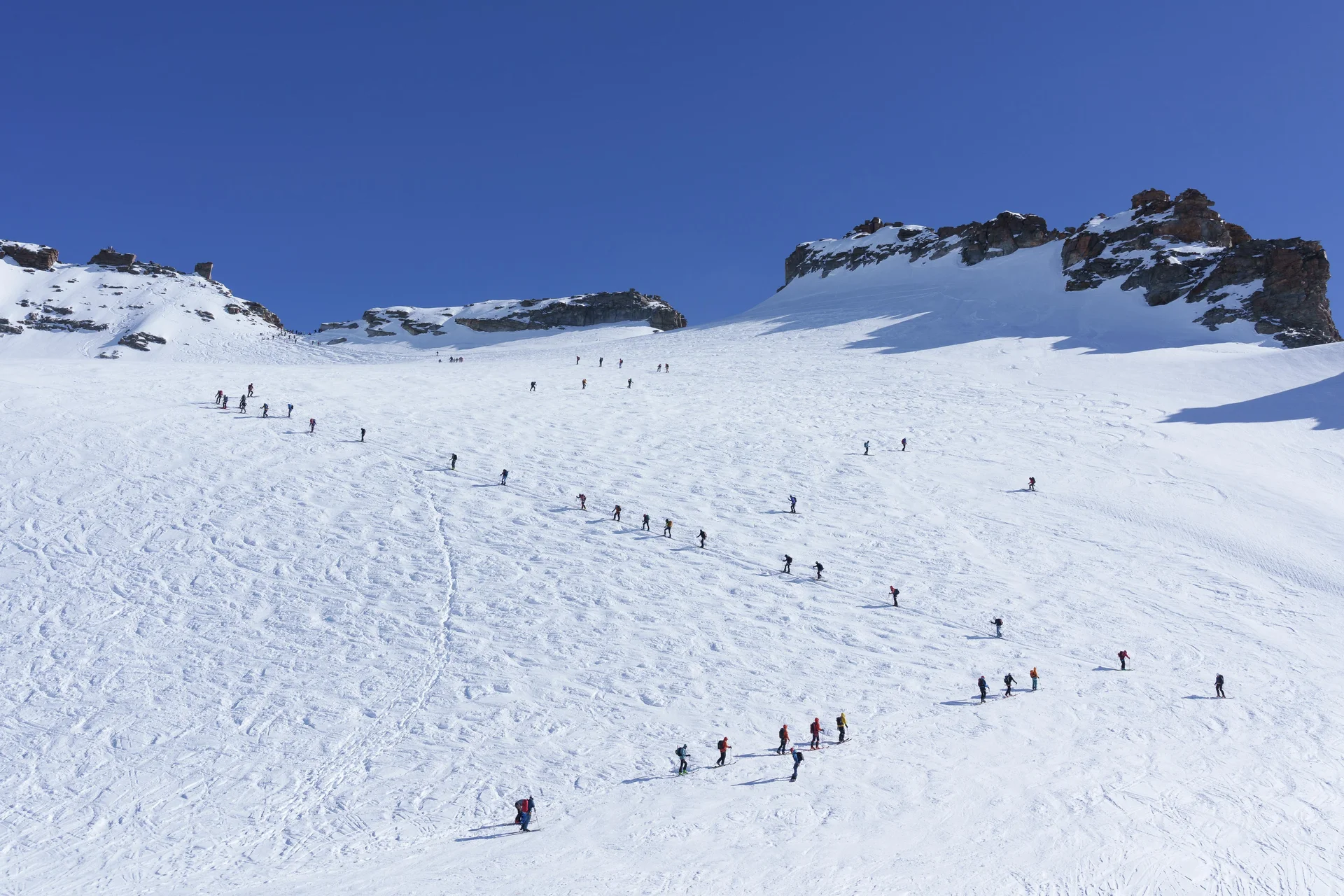 Große Gruppe von Menschen wandert in einer langen Reihe auf schneebedecktem Berg unter klarem blauem Himmel | © DAV-FN / R. Gersten u. L. Chr. Fischer