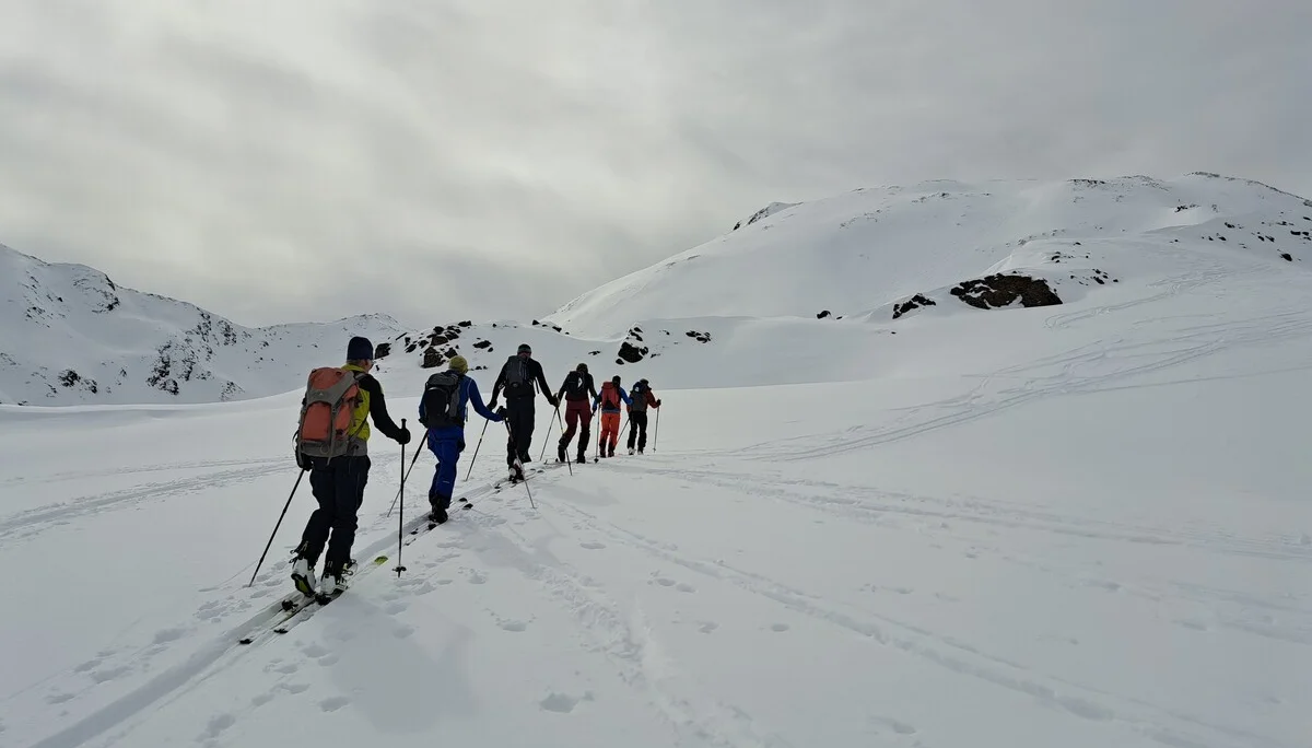 Sechs Skitourengeher in einer Reihe steigen auf schneebedecktem Berg unter bewölktem Himmel auf | © DAV-FN / R.Lebedeff, D. Lexen