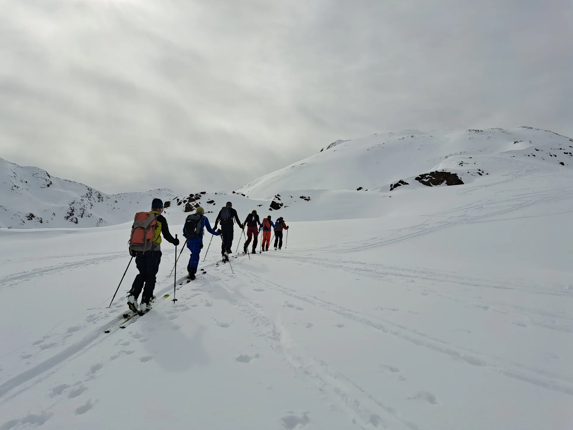 Sechs Skitourengeher in einer Reihe steigen auf schneebedecktem Berg unter bewölktem Himmel auf | © DAV-FN / R.Lebedeff, D. Lexen