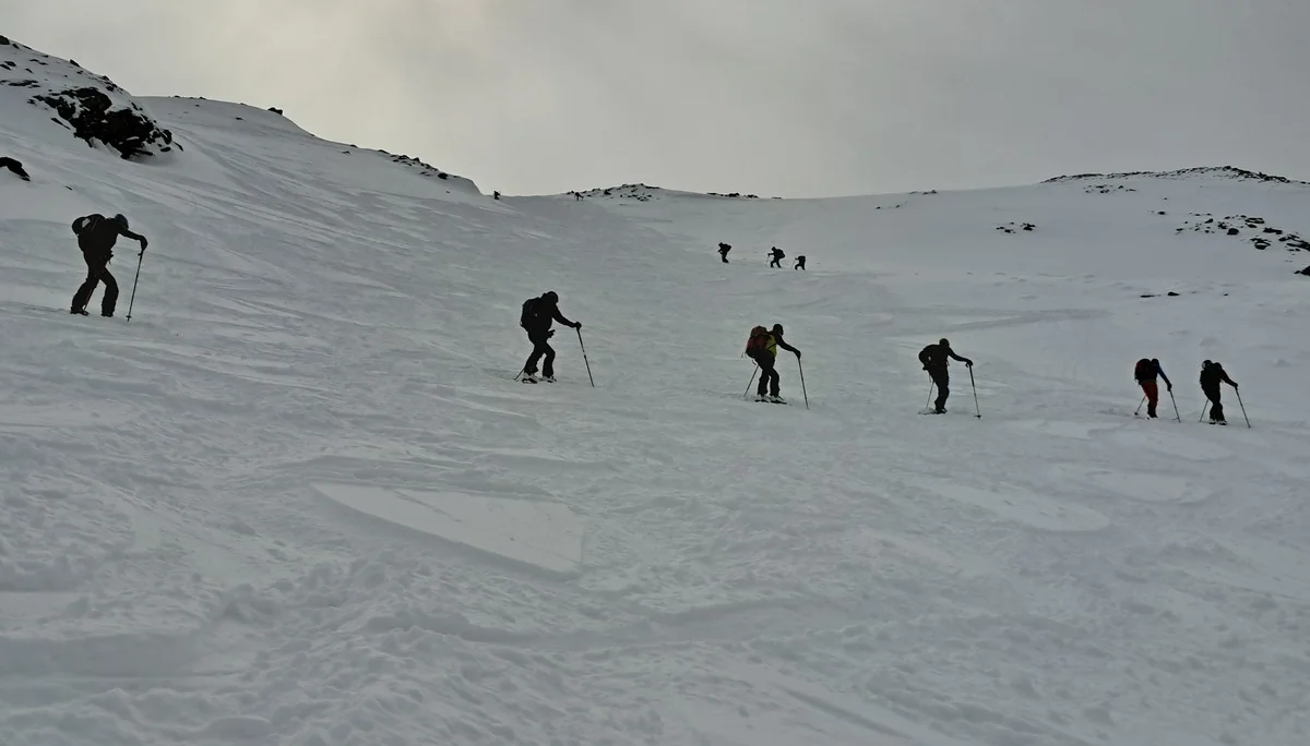 Sechs Skifahrer steigen mit Skistöcken einen schneebedeckten Hang unter bewölktem Himmel hinauf | © DAV-FN / R.Lebedeff, D. Lexen