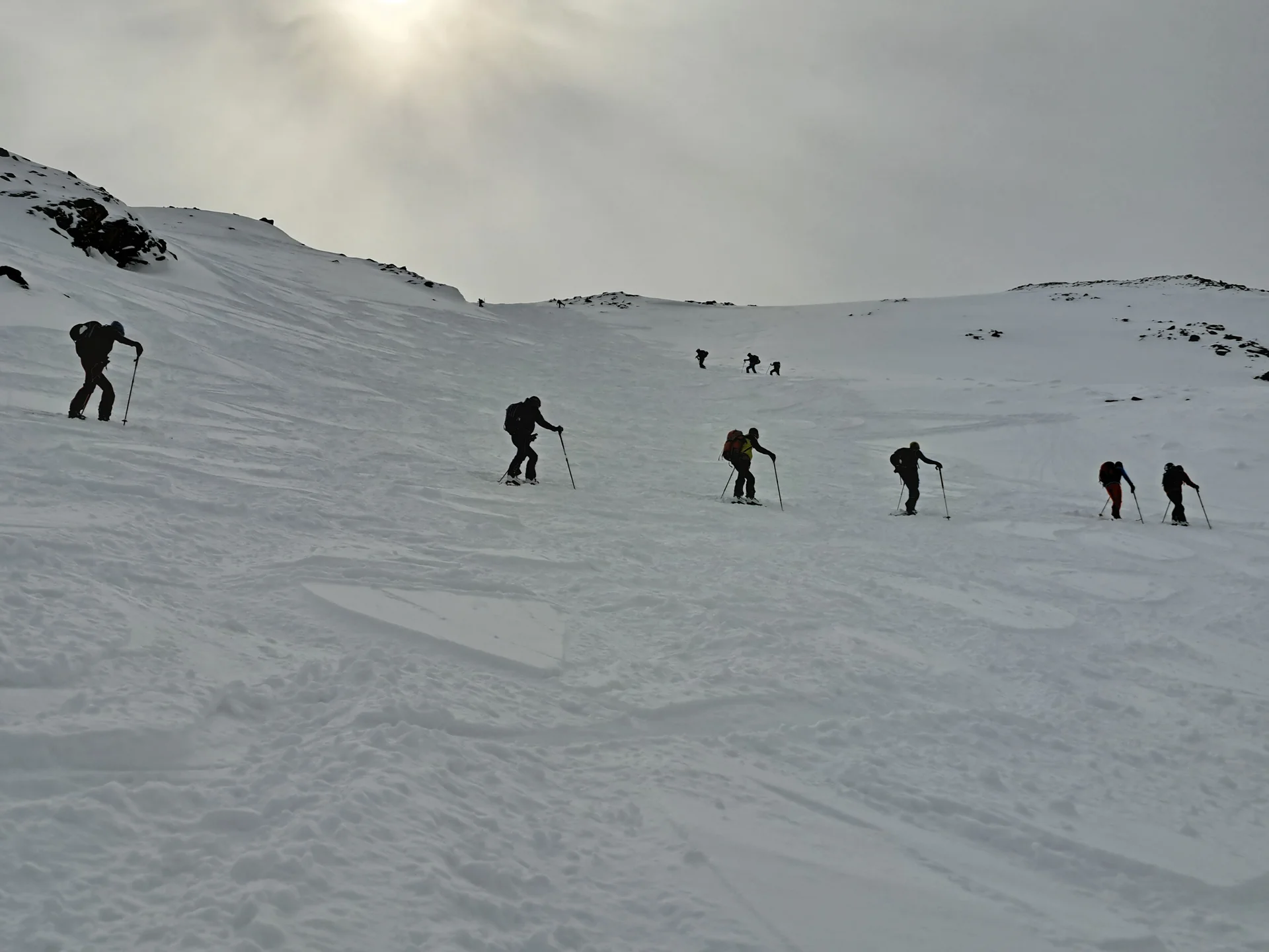 Sechs Skifahrer steigen mit Skistöcken einen schneebedeckten Hang unter bewölktem Himmel hinauf | © DAV-FN / R.Lebedeff, D. Lexen