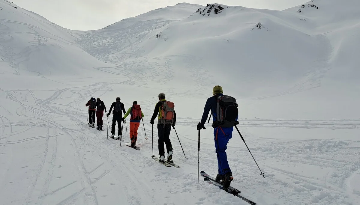 Sechs Skitourengeher mit Rucksäcken steigen in einer Reihe einen schneebedeckten Berg hinauf | © DAV-FN / R.Lebedeff, D. Lexen
