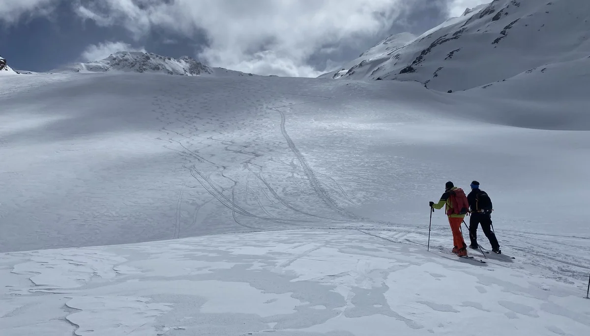 Zwei Skifahrer mit Ausrüstung stehen auf schneebedecktem Hang unter bewölktem Himmel in den Bergen | © DAV-FN / R.Lebedeff, D. Lexen