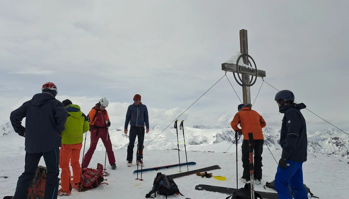 Sechs Skifahrer in bunter Winterkleidung stehen am Gipfelkreuz auf einem schneebedeckten Berg mit Skiern und Stöcken im Schnee | © DAV-FN / R.Lebedeff, D. Lexen