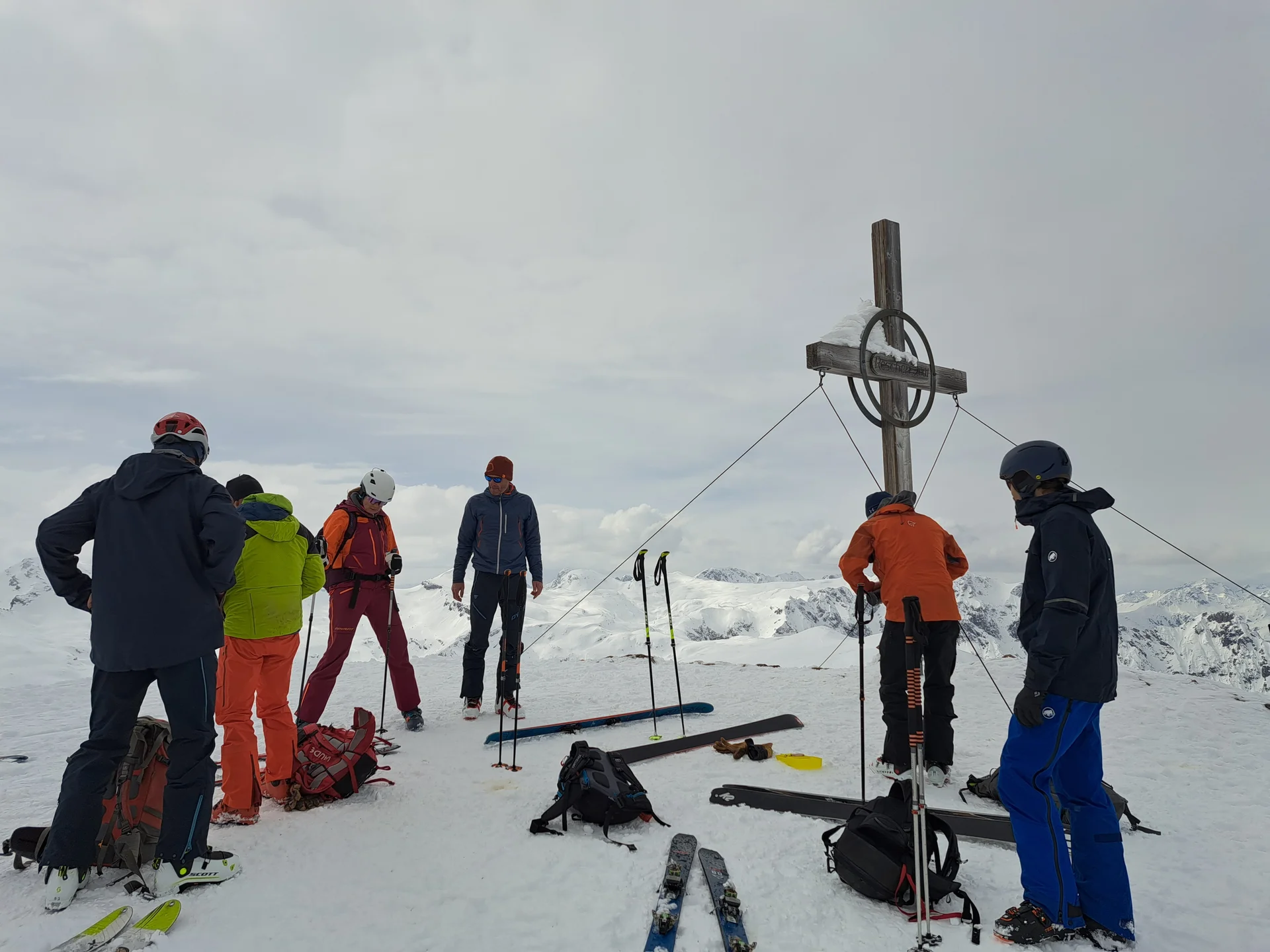 Sechs Skifahrer in bunter Winterkleidung stehen am Gipfelkreuz auf einem schneebedeckten Berg mit Skiern und Stöcken im Schnee | © DAV-FN / R.Lebedeff, D. Lexen