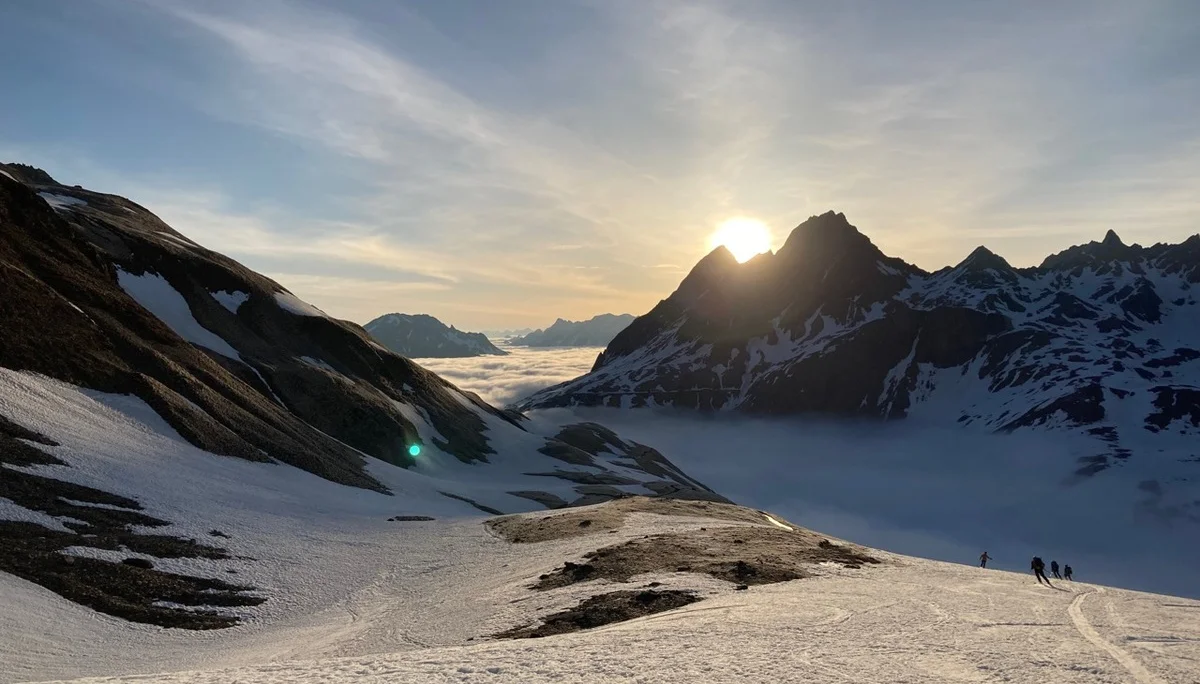 Abfahrende Skifahrer in ein nebelverhangenes Tal gegen die untergehenden Sonne | © DAV-FN / P. Schäfer