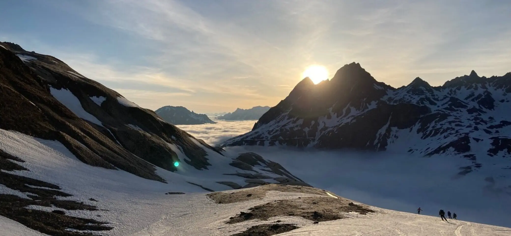 Abfahrende Skifahrer in ein nebelverhangenes Tal gegen die untergehenden Sonne | © DAV-FN / P. Schäfer