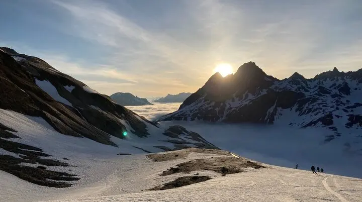 Abfahrende Skifahrer in ein nebelverhangenes Tal gegen die untergehenden Sonne | © DAV-FN / P. Schäfer